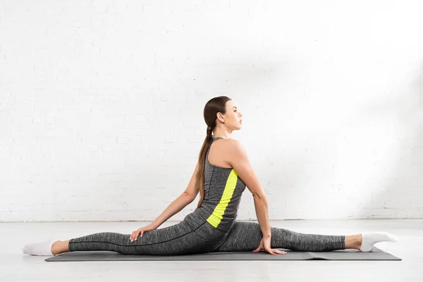 Vue latérale de la fille flexible et sportive faisant ficelle sur tapis de fitness — Photo de stock