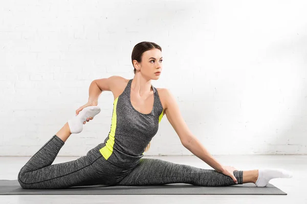 Flexible and sportive woman doing twine and stretching on fitness mat — Stock Photo