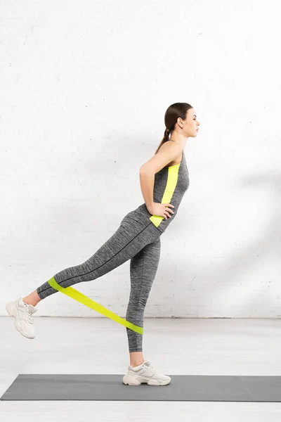 Ragazza sportiva con mano sull'anca esercizio con fascia di resistenza sul tappeto fitness — Foto stock