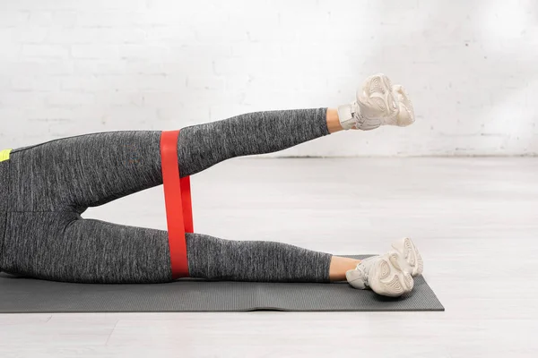 Cropped view of sportive woman exercising with resistance band on fitness mat — Stock Photo