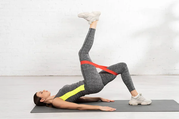 Vue latérale de la femme sportive faisant de l'exercice avec bande de résistance sur tapis de fitness — Photo de stock