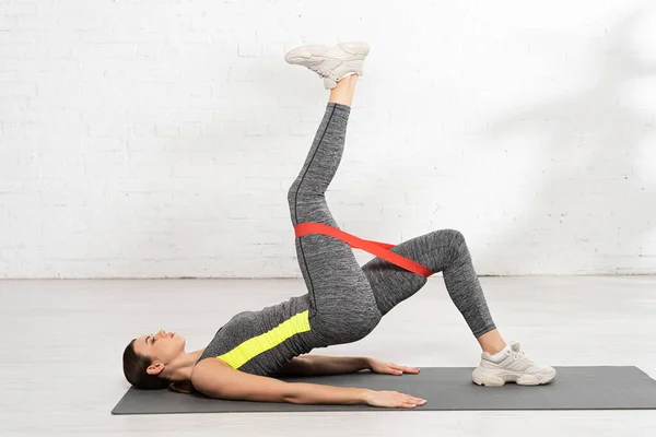 Vue latérale de la femme sportive faisant de l'exercice avec bande de résistance sur tapis de fitness — Photo de stock