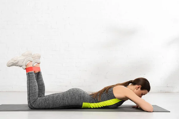 Mujer deportiva acostada en la alfombra de fitness y haciendo ejercicio con banda de resistencia - foto de stock