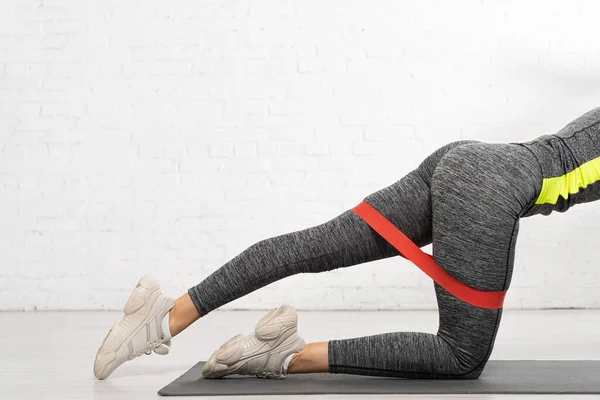 Vista recortada de la mujer deportiva de pie sobre la rodilla y haciendo ejercicio con banda de resistencia - foto de stock