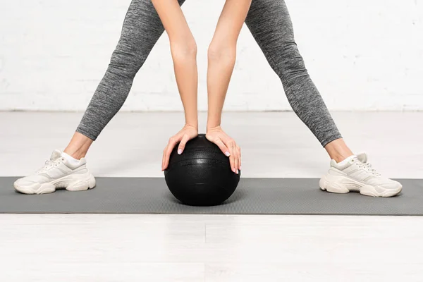 Cropped view of young woman in sportswear working out with black ball — Stock Photo