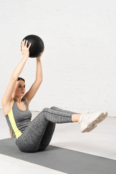 Attraktive Sportlerin in Sportbekleidung, die mit Ball auf Fitnessmatte trainiert — Stockfoto