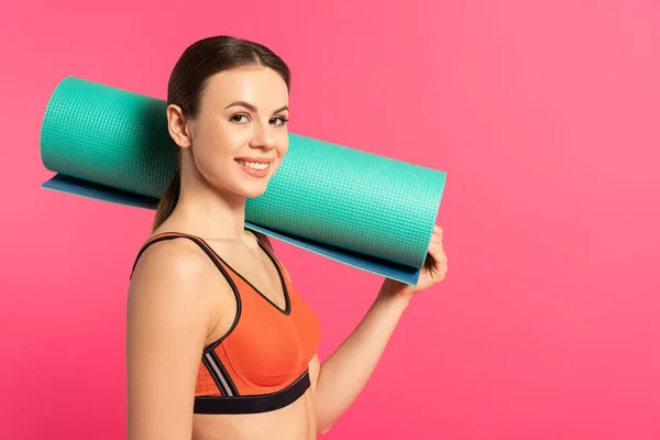 Happy sportswoman holding fitness mat isolated on pink — Stock Photo