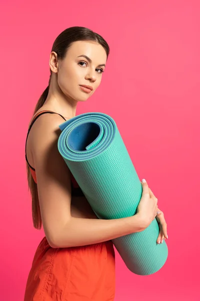 Привлекательная спортсменка держит фитнес коврик изолирован на розовый — стоковое фото