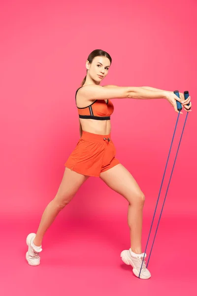 Athletic woman in sportswear exercising with skipping rope on pink — Stock Photo
