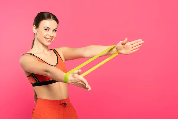 Deportista feliz haciendo ejercicio con banda de resistencia aislada en rosa - foto de stock