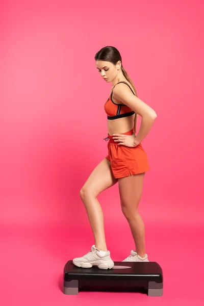 Sportswoman with hand on hip exercising on step platform on pink — Stock Photo