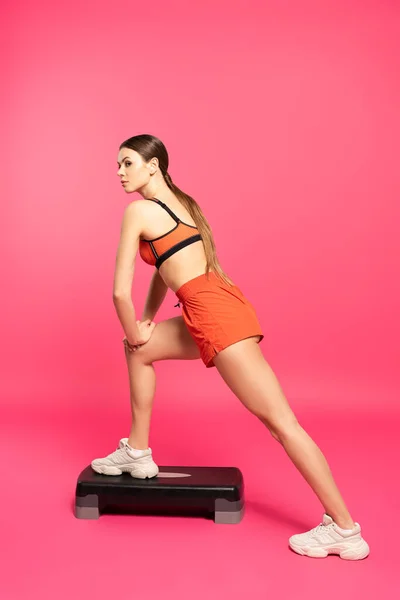 Спортивная женщина тренирующаяся на ступенчатой платформе на розовом — стоковое фото