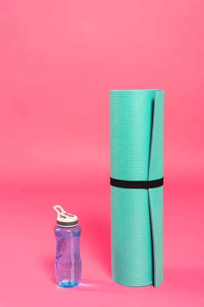 Bouteille de sport avec de l'eau près tapis de fitness sur rose — Photo de stock