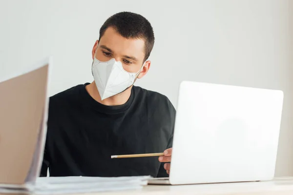 Selektiver Fokus der Freiberuflerin in medizinischer Maske beim Blick auf Ordner in Laptopnähe — Stockfoto