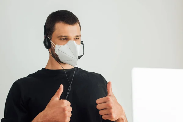 Selective focus of operator in medical mask and headset showing thumbs up while having video call at home — Stock Photo