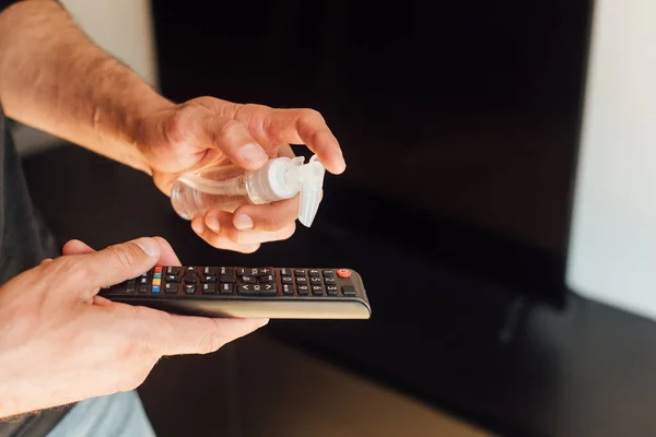 Cropped view of man holding bottle with sanitizer near remote controller — Stock Photo