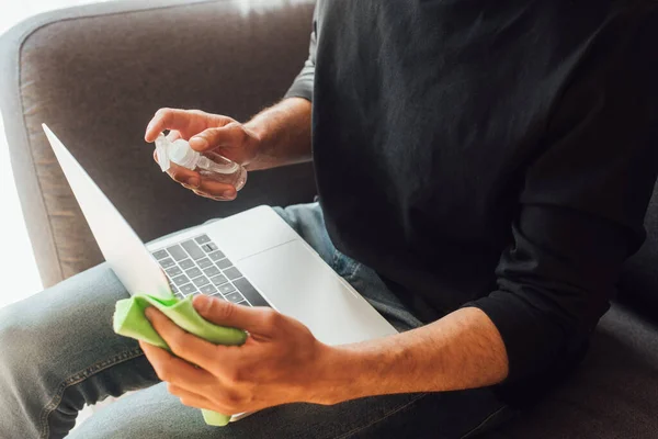 Vista cortada do homem segurando garrafa com líquido antibacteriano perto do laptop — Fotografia de Stock