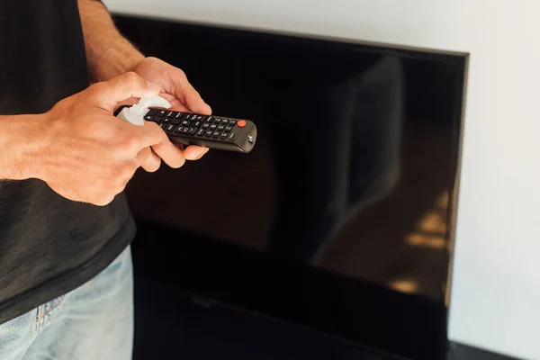 Abgeschnittene Ansicht eines Mannes, der eine Flasche mit antibakterieller Flüssigkeit in der Nähe der Fernbedienung hält — Stockfoto