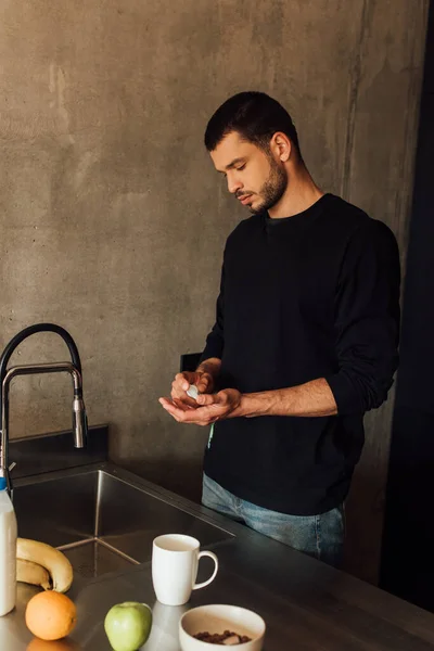 Bearded man holding bottle with hand sanitizer in kitchen — Stock Photo