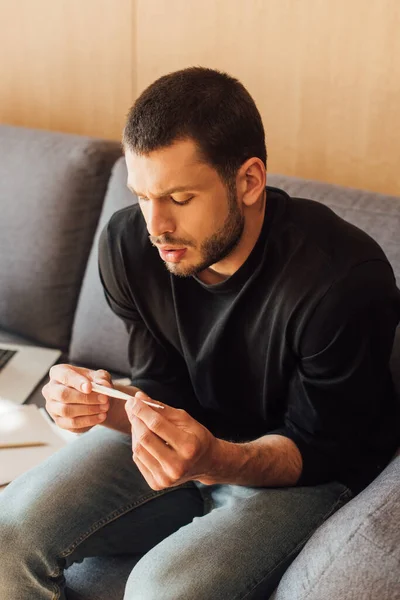 Uomo malato e barbuto guardando il termometro digitale a casa — Foto stock
