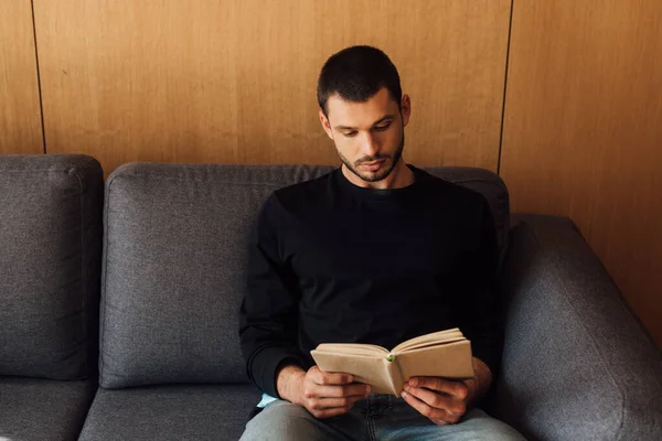 Gutaussehender und bärtiger Mann liest Buch im Wohnzimmer — Stockfoto