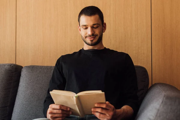 Hombre feliz y barbudo leyendo libro en la sala de estar - foto de stock