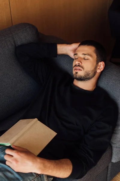 Libro sobre el hombre barbudo y guapo durmiendo en la sala de estar - foto de stock