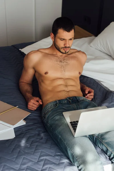 Barbudo y sin camisa freelancer acostado en la cama y mirando a la computadora portátil - foto de stock