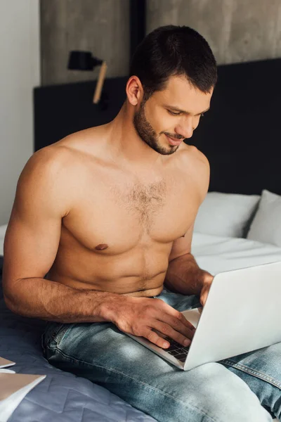 Feliz y sin camisa freelancer utilizando el ordenador portátil en el dormitorio - foto de stock