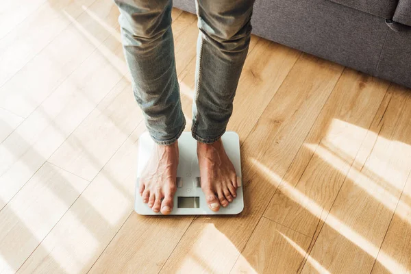 Vue recadrée de l'homme debout sur des balances à la maison — Photo de stock