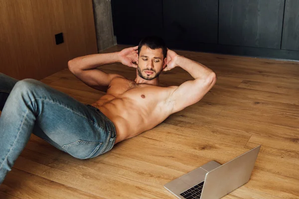 Hombre musculoso haciendo ejercicio mientras ve el entrenamiento en línea en el ordenador portátil - foto de stock