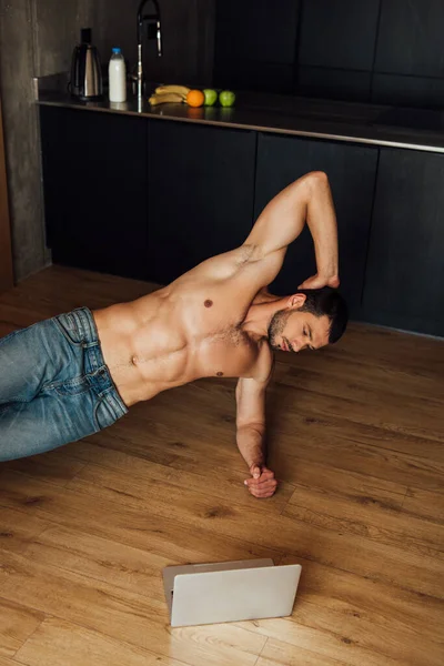 Hombre sin camisa haciendo ejercicio mientras ve el entrenamiento en línea en el ordenador portátil - foto de stock