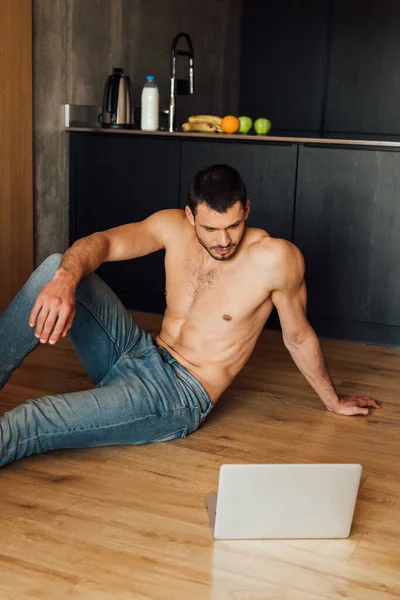 Hombre sin camisa sentado en el suelo y viendo el entrenamiento en línea en el ordenador portátil - foto de stock