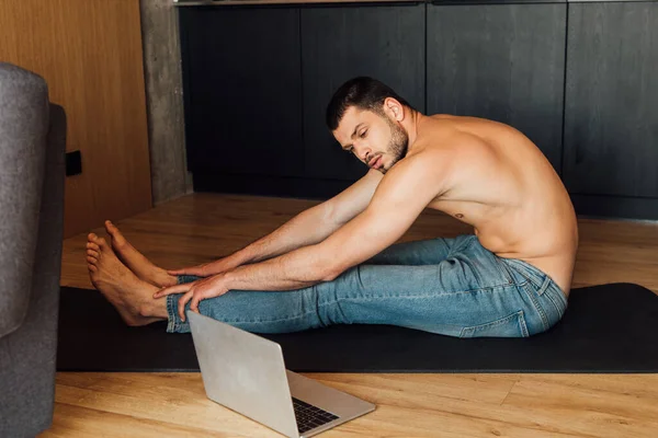 Mann ohne Hemd übt auf Yogamatte und schaut sich Online-Yoga-Training am Laptop an — Stockfoto