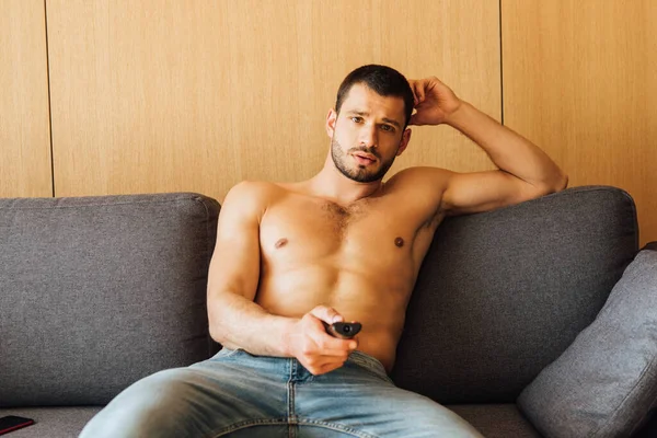 Shirtless man in jeans watching movie and holding remote controller — Stock Photo