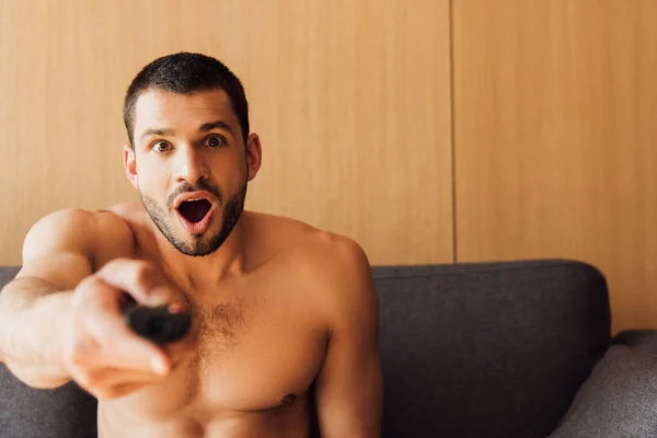 Enfoque selectivo del hombre sorprendido y sin camisa que sostiene el mando a distancia - foto de stock