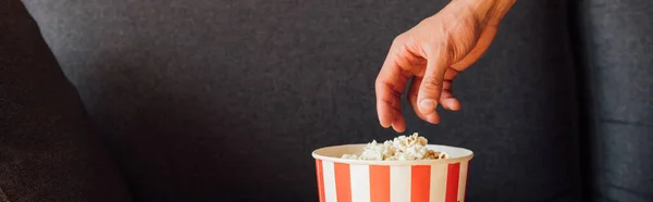 Panoramic crop of man reaching popcorn in bucket — Stock Photo