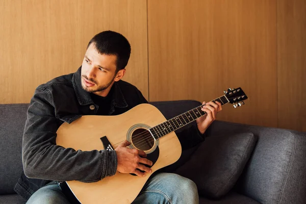 Uomo barbuto suonare la chitarra acustica in soggiorno — Foto stock