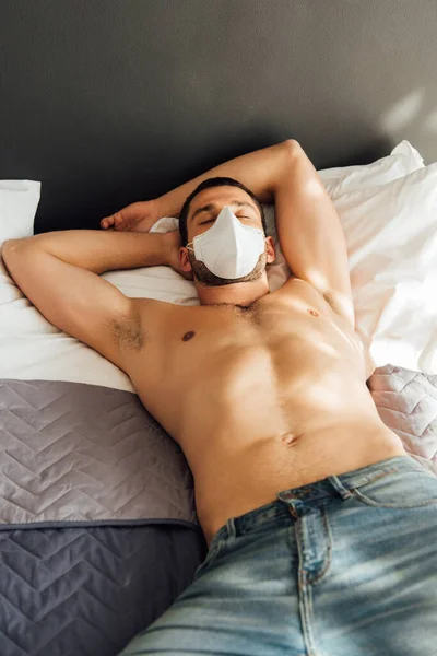 Мужчина без рубашки в медицинской маске спит на кровати — стоковое фото
