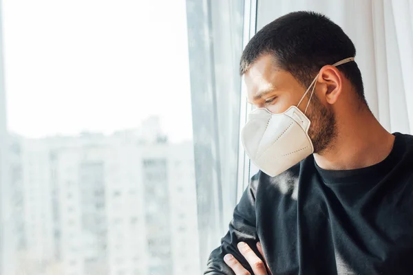 Мужчина в медицинской маске стоит у окна дома — Stock Photo