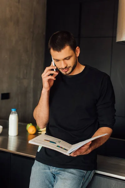 Hombre guapo hablando en el teléfono inteligente mientras sostiene gráficos y gráficos - foto de stock