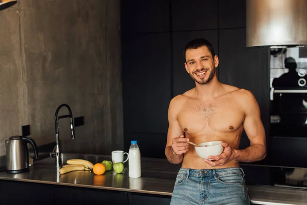 Homme torse nu souriant tout en tenant bol avec des flocons de maïs dans la cuisine — Photo de stock