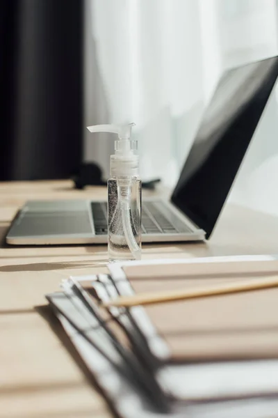 Selective focus of bottle with sanitizer near laptop and folder on table — Stock Photo