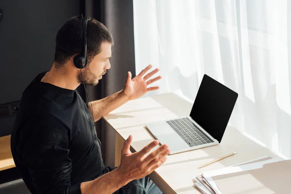 Operatore emotivo in auricolare gesticolare vicino al computer portatile con schermo vuoto — Foto stock