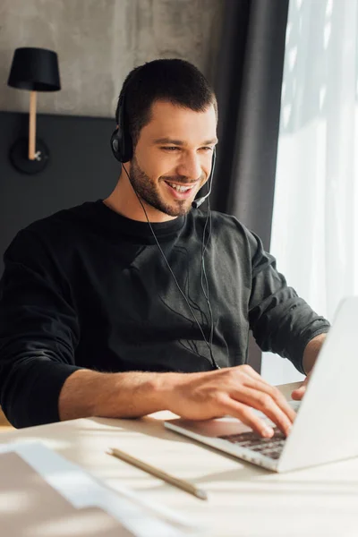 Foco seletivo do operador feliz no fone de ouvido usando laptop em casa — Fotografia de Stock