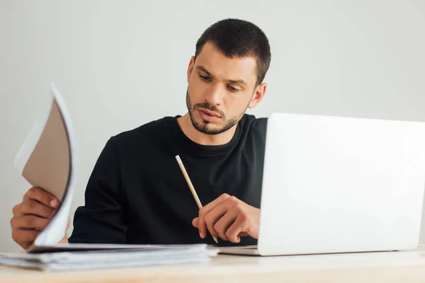 Selective focus of bearded blogger looking at folder near laptop — Stock Photo