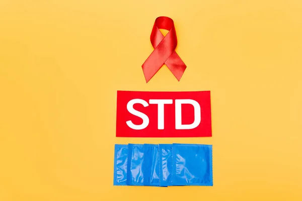 Fita vermelha como consciência hiv perto de letras std e preservativos isolados em laranja — Fotografia de Stock
