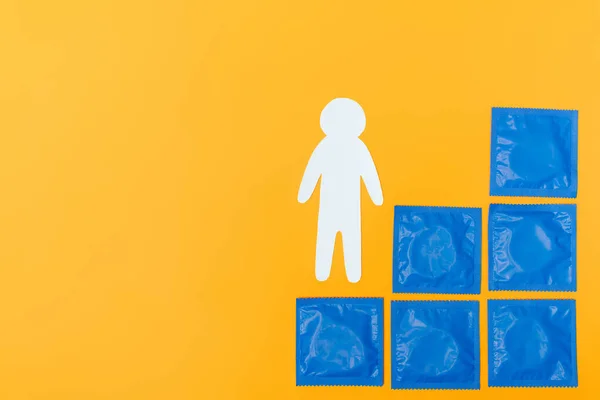 Вид сверху на голубые упаковки с презервативами рядом с бумагой человека изолированы на оранжевый — стоковое фото