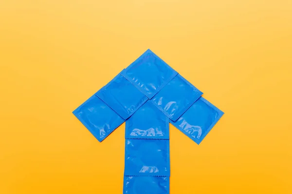 Top view of blue arrow from packs with condoms isolated on orange — Stock Photo