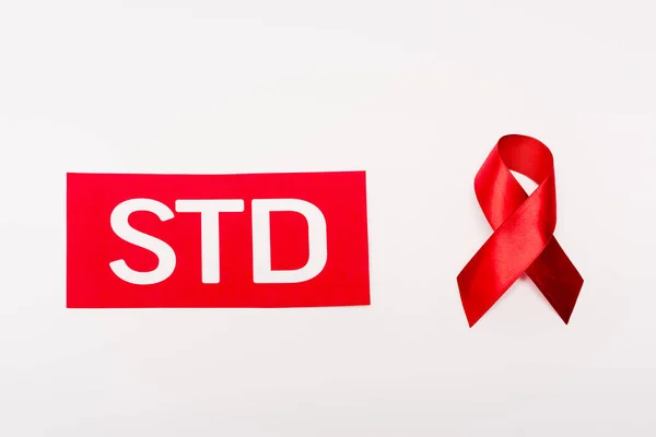 Top view of red ribbon near paper with std lettering isolated on white — Stock Photo